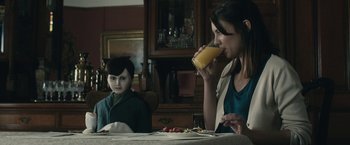 Movie still from “The Boy” (2016), directed by William Brent Bell – A woman and a boy sitting at a table drinking orange juice; Medium shot, Over the shoulder angle