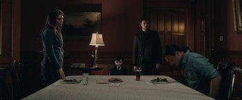 Movie still from “The Boy” (2016), directed by William Brent Bell – A man standing at a dinner table with a young boy; Medium shot, Over the shoulder angle
