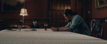 Movie still from “The Boy” (2016), directed by William Brent Bell – A man sitting at a dining table with a boy; Medium shot, Over the shoulder angle
