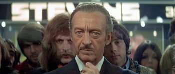 Movie still from “The Brain” (1969), directed by Gérard Oury – An older man in a suit and tie with three other men behind him; Close Up shot, Over the shoulder angle