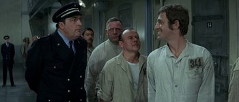 Movie still from “The Brain” (1969), directed by Gérard Oury – A group of men standing next to each other in a room; Medium shot, Over the shoulder angle