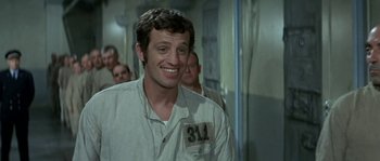 Movie still from “The Brain” (1969), directed by Gérard Oury – A man in a prison uniform smiling for the camera; Close Up shot, High angle