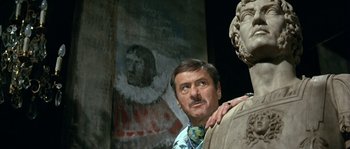 Movie still from “The Brain” (1969), directed by Gérard Oury – A man standing in front of a painting of an old man; Close Up shot, Low angle