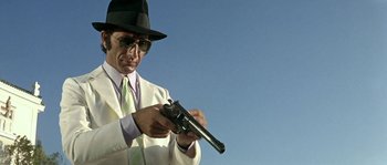 Movie still from “The Brain” (1969), directed by Gérard Oury – A man in a white suit and hat holding a gun; Medium shot, Low angle