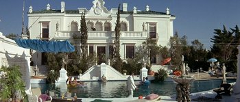 Movie still from “The Brain” (1969), directed by Gérard Oury – People are swimming in a pool in front of a large mansion; Extreme Wide shot, Low angle