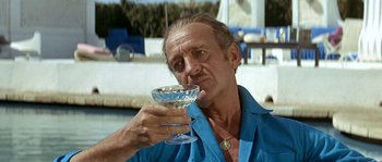 Movie still from “The Brain” (1969), directed by Gérard Oury – A man holding a wine glass in his right hand; Medium shot, Low angle