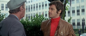 Movie still from “The Brain” (1969), directed by Gérard Oury – A man in a brown leather jacket talking to another man; Medium shot, Over the shoulder angle