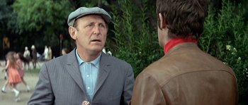 Movie still from “The Brain” (1969), directed by Gérard Oury – A man wearing a hat and a suit talking to another man; Close Up shot, Over the shoulder angle