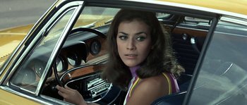 Movie still from “The Brain” (1969), directed by Gérard Oury – A woman sitting in the driver's seat of a car; Close Up shot, Over the shoulder angle