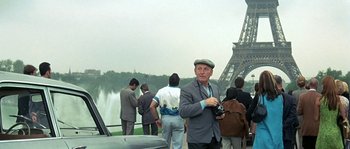 Movie still from “The Brain” (1969), directed by Gérard Oury – A man in a suit and a hat standing in front of a group of people; Wide shot, Over the shoulder angle