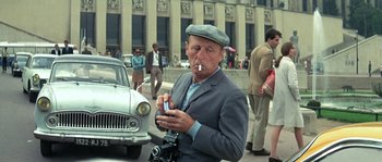 Movie still from “The Brain” (1969), directed by Gérard Oury – An older man smoking a cigarette while holding a cell phone; Medium shot, Low angle