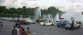 Movie still from “The Brain” (1969), directed by Gérard Oury – A group of cars parked in front of a fountain; Extreme Wide shot, High angle