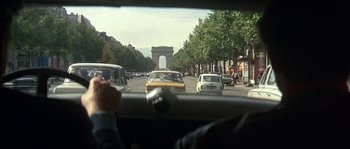 Movie still from “The Brain” (1969), directed by Gérard Oury – Cars driving down a street with a view of the arc de triomphe in the background; Wide shot, Over the shoulder angle