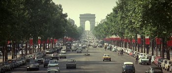 Movie still from “The Brain” (1969), directed by Gérard Oury – A street filled with lots of traffic next to trees; Extreme Wide shot, High angle