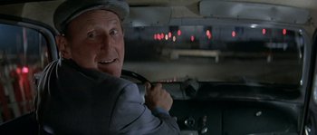 Movie still from “The Brain” (1969), directed by Gérard Oury – An older man in a suit and hat holding a steering wheel in a car; Close Up shot, Over the shoulder angle