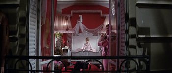 Movie still from “The Brain” (1969), directed by Gérard Oury – A woman sitting on top of a bed next to a man in a suit; Wide shot, Low angle