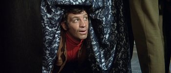 Movie still from “The Brain” (1969), directed by Gérard Oury – A man hides his face under a curtain; Medium shot, Low angle