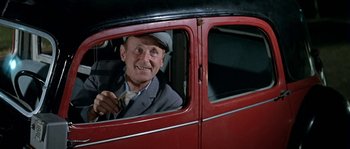 Movie still from “The Brain” (1969), directed by Gérard Oury – An older man sitting in the driver's seat of an old car; Medium shot, Low angle