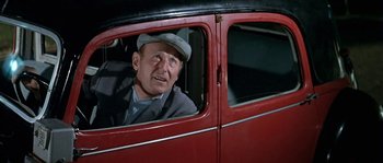 Movie still from “The Brain” (1969), directed by Gérard Oury – An older man sitting in the driver's seat of an old car; Medium shot, High angle