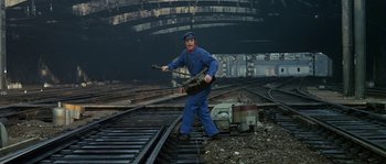 Movie still from “The Brain” (1969), directed by Gérard Oury – A man holding a guitar on top of train tracks; Wide shot, High angle