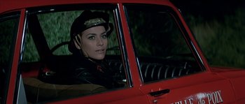 Movie still from “The Brain” (1969), directed by Gérard Oury – A woman sitting in the driver's seat of a red car; Close Up shot, High angle