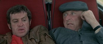 Movie still from “The Brain” (1969), directed by Gérard Oury – A man sitting next to another man on a train; Close Up shot, High angle