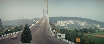 Movie still from “The Brain” (1969), directed by Gérard Oury – A road with a bridge in the middle of the road; Extreme Wide shot, High angle