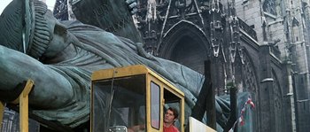 Movie still from “The Brain” (1969), directed by Gérard Oury – A man riding on the back of a yellow construction vehicle; Wide shot, Low angle