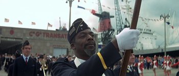 Movie still from “The Brain” (1969), directed by Gérard Oury – A man in a military uniform is holding a flag; Medium shot, Low angle