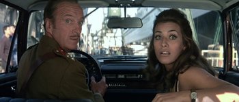 Movie still from “The Brain” (1969), directed by Gérard Oury – A man and a woman sitting in the back seat of a car; Close Up shot, Over the shoulder angle