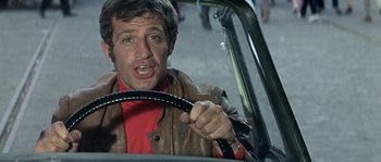 Movie still from “The Brain” (1969), directed by Gérard Oury – A man in a leather jacket driving a car; Close Up shot, Low angle