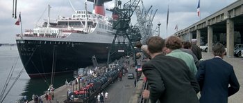 Movie still from “The Brain” (1969), directed by Gérard Oury – A group of people standing next to a large ship; Extreme Wide shot, High angle