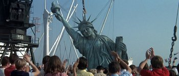 Movie still from “The Brain” (1969), directed by Gérard Oury – A group of people standing around a statue of liberty; Extreme Wide shot, Low angle