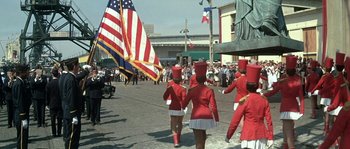Movie still from “The Brain” (1969), directed by Gérard Oury – A group of women in red marching down a street; Wide shot, Low angle