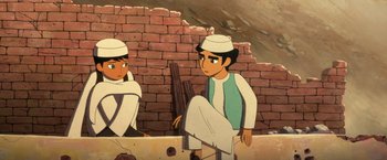 Movie still from “The Breadwinner” (2017), directed by Nora Twomey – A cartoon of two men sitting next to a brick wall; Medium shot, Over the shoulder angle