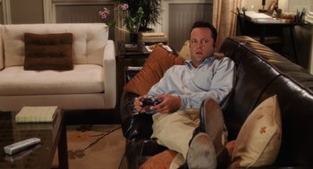 Movie still from “The Break-Up” (2006), directed by Peyton Reed – A man sitting in a chair holding a remote control; Medium shot, High angle