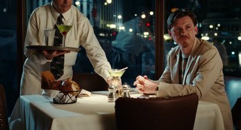 Movie still from “The Break-Up” (2006), directed by Peyton Reed – A man sitting at a table with a drink in front of him; Medium shot, Over the shoulder angle