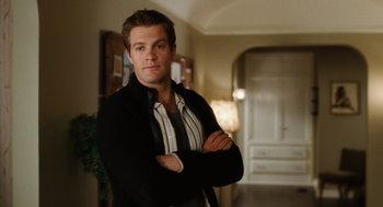 Movie still from “The Break-Up” (2006), directed by Peyton Reed – A man standing with his arms crossed in a room; Medium shot, Over the shoulder angle