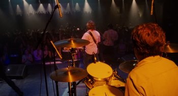 Movie still from “The Break-Up” (2006), directed by Peyton Reed – A man playing drums in front of an audience; Medium shot, High angle