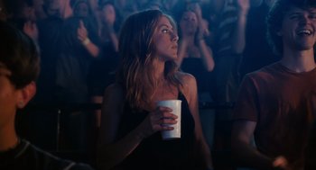 Movie still from “The Break-Up” (2006), directed by Peyton Reed – A woman holding a cup in front of an audience; Medium shot, Over the shoulder angle