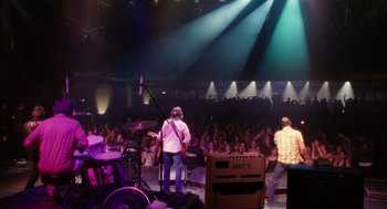 Movie still from “The Break-Up” (2006), directed by Peyton Reed – A man playing drums in front of an audience; Wide shot, High angle