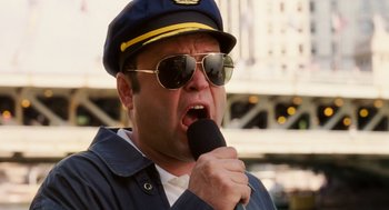 Movie still from “The Break-Up” (2006), directed by Peyton Reed – A man wearing a hat and sunglasses is holding a microphone; Close Up shot, Low angle