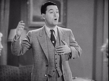 Movie still from “The Broadway Melody” (1929), directed by Harry Beaumont – A man wearing a suit and tie while holding his hands up to his chest; Medium shot, High angle