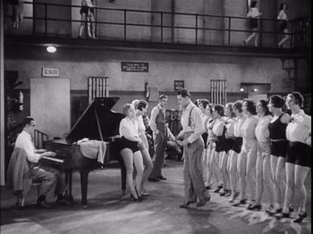 Movie still from “The Broadway Melody” (1929), directed by Harry Beaumont – A black and white photo of a group of people standing around a piano; Wide shot, High angle