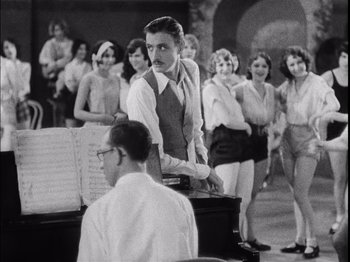 Movie still from “The Broadway Melody” (1929), directed by Harry Beaumont – A man standing next to an orchestra with a group of women; Medium shot, High angle