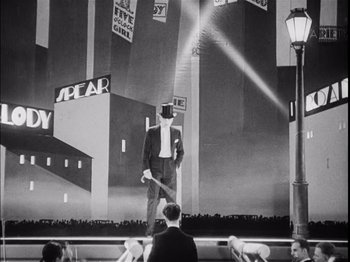Movie still from “The Broadway Melody” (1929), directed by Harry Beaumont – A man in a suit and top hat on a stage; Wide shot, Low angle