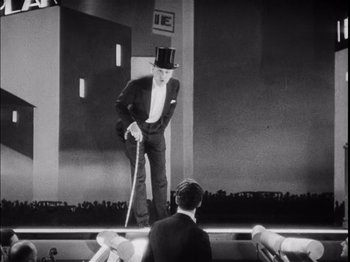 Movie still from “The Broadway Melody” (1929), directed by Harry Beaumont – A man in a top hat and cane standing on a stage; Wide shot, Low angle