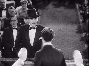 Movie still from “The Broadway Melody” (1929), directed by Harry Beaumont – A man in a black suit and a black hat is talking to a man in a black suit and a black hat; Medium shot, Over the shoulder angle