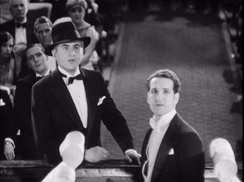 Movie still from “The Broadway Melody” (1929), directed by Harry Beaumont – Two men in tuxedos standing next to each other in front of a crowd of onlookers; Medium shot, Low angle