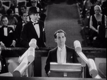 Movie still from “The Broadway Melody” (1929), directed by Harry Beaumont – A man in a suit and tie standing in front of a microphone; Medium shot, Low angle